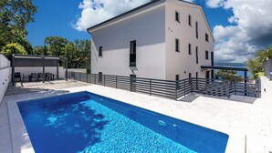 Ein modernes Gebäude mit Schwimmbad, Sitzgelegenheiten im Freien und Meerblick.