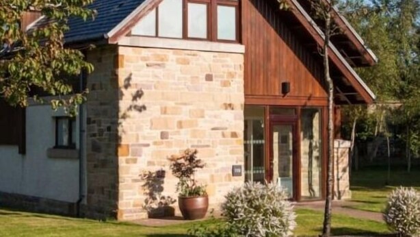 Une maison en pierre à deux étages, avec un toit à pignon, de grandes fenêtres et une porte d’entrée.