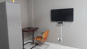 Una habitación con armario, una mesita pequeña, una silla y televisor montado en la pared.