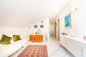 A room with a white sofa, a patterned rug, a wooden cabinet, and a white console table.