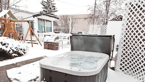 Una vasca idromassaggio in un giardino innevato con un pontile in legno e un'altalena.
