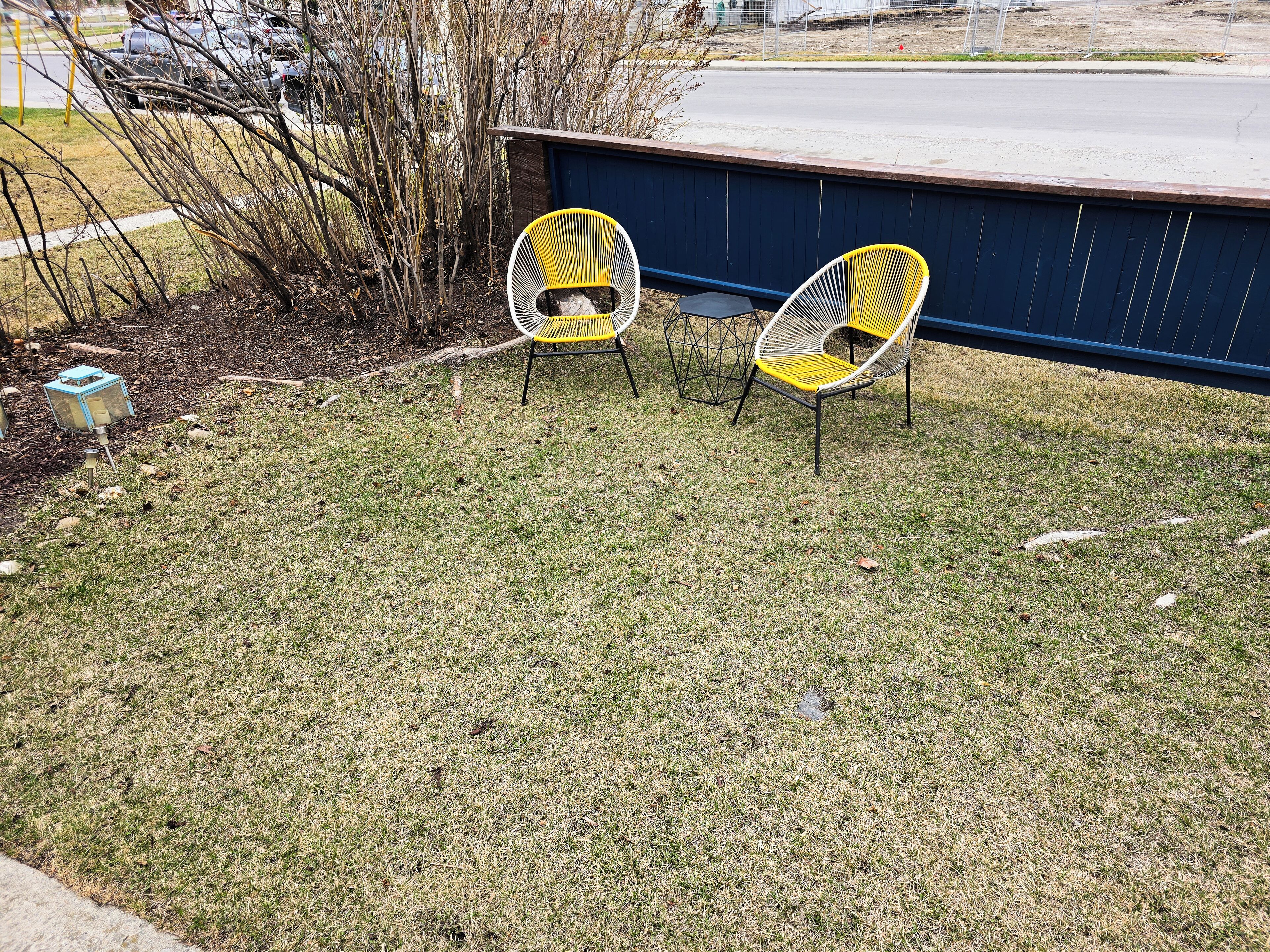 A grassy outdoor area with two yellow chairs and a blue wall in the background.