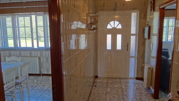 Un pasillo con suelo de baldosas, una puerta blanca con paneles de vidrio y una ventana con vistas a follaje.