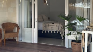 A room with a bed, a wicker chair, a potted plant, and a glass door leading to another room. - Sol Villas Gili Air  (Gili Air)