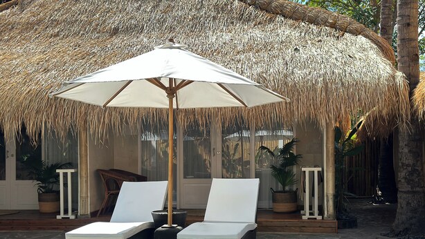 A poolside area with two lounge chairs and a large umbrella, surrounded by tropical plants and a thatched roof structure. - Sol Villas Gili Air  (Gili Air)