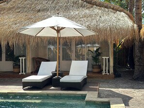 A poolside area with two lounge chairs and a large umbrella, surrounded by tropical plants and a thatched roof structure. - Sol Villas Gili Air  (Gili Air)