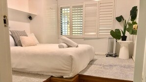 Un dormitorio con cama, un radiador, una planta en maceta y una ventana con persianas.