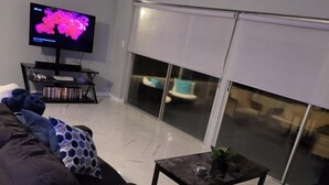 A living room with a black sofa, a TV, a bookshelf, and a sliding glass door to the outside. - Cozy 3-bedroom house in peaceful Spring Hill with WiFi, AC. Sleeps up to 15 (Spring Hill)