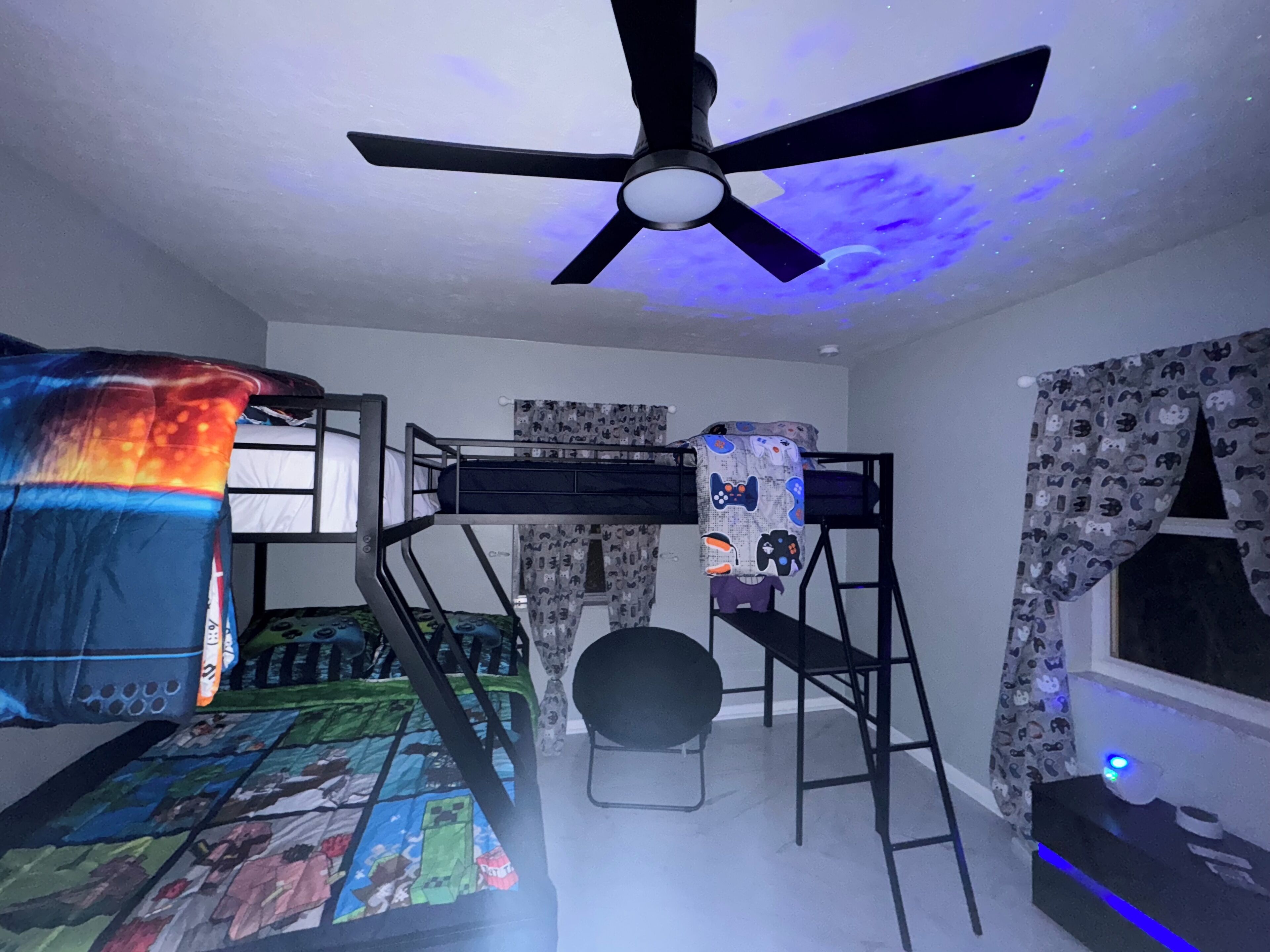 A room with bunk beds, a ceiling fan, and a window with curtains.