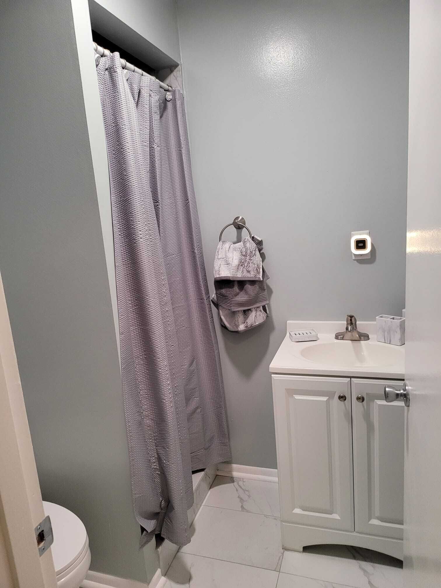 A bathroom with a shower curtain, a towel rack with a towel, a toilet, and a sink with a soap dispenser.