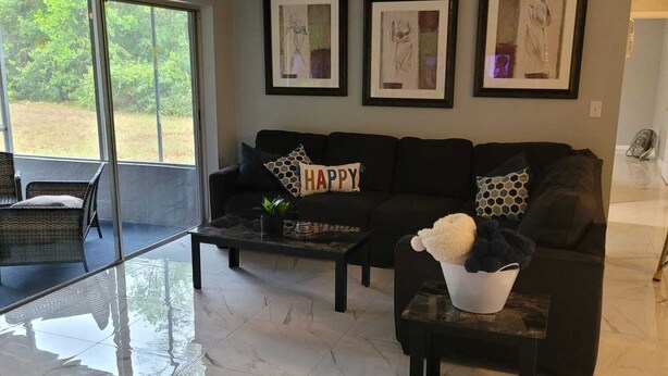 A modern living room with a black sofa, a coffee table, and a large window. - Cozy 3-bedroom house in peaceful Spring Hill with WiFi, AC. Sleeps up to 15 (Spring Hill)