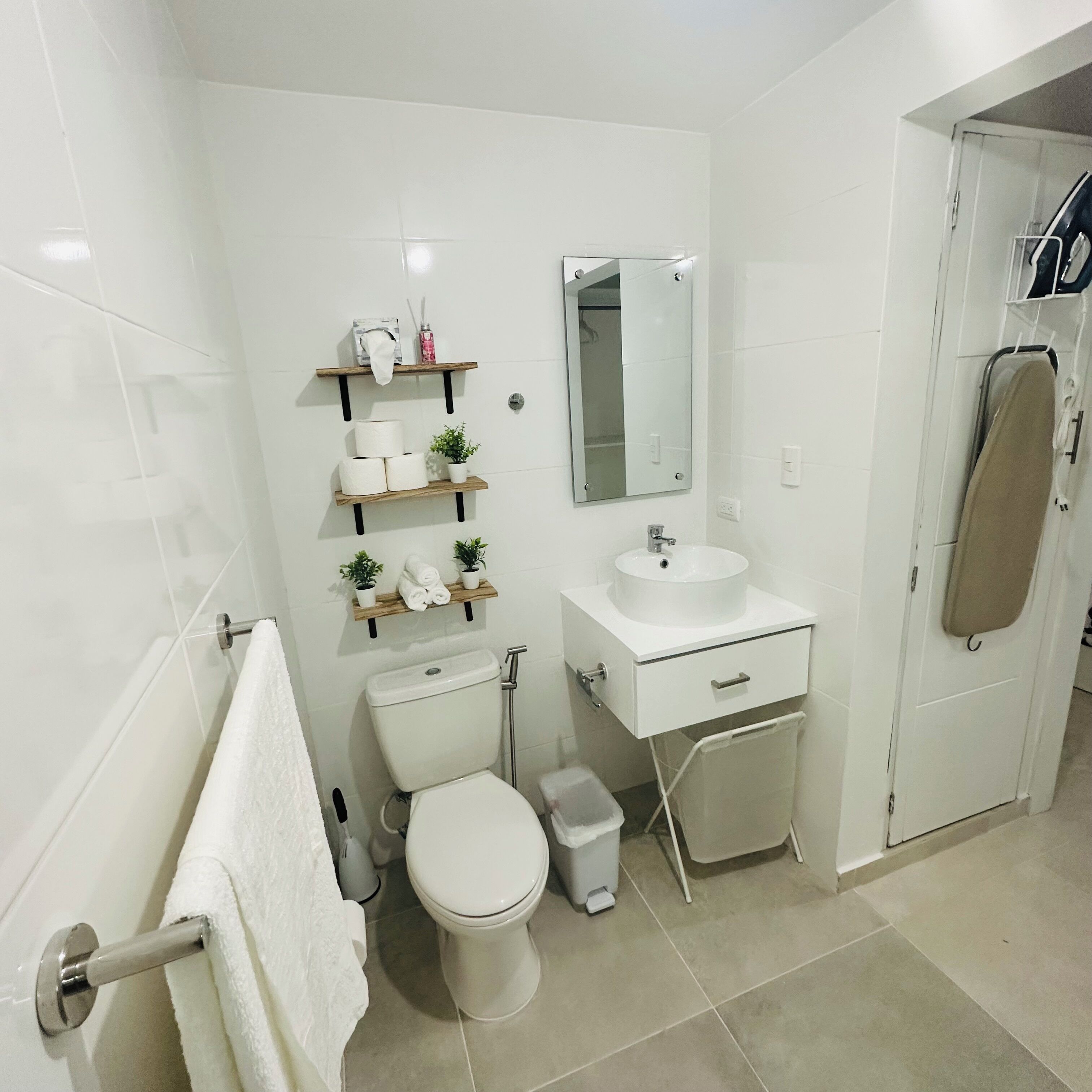 A modern bathroom with white fixtures, a toilet, a sink, a mirror, and a shower area.