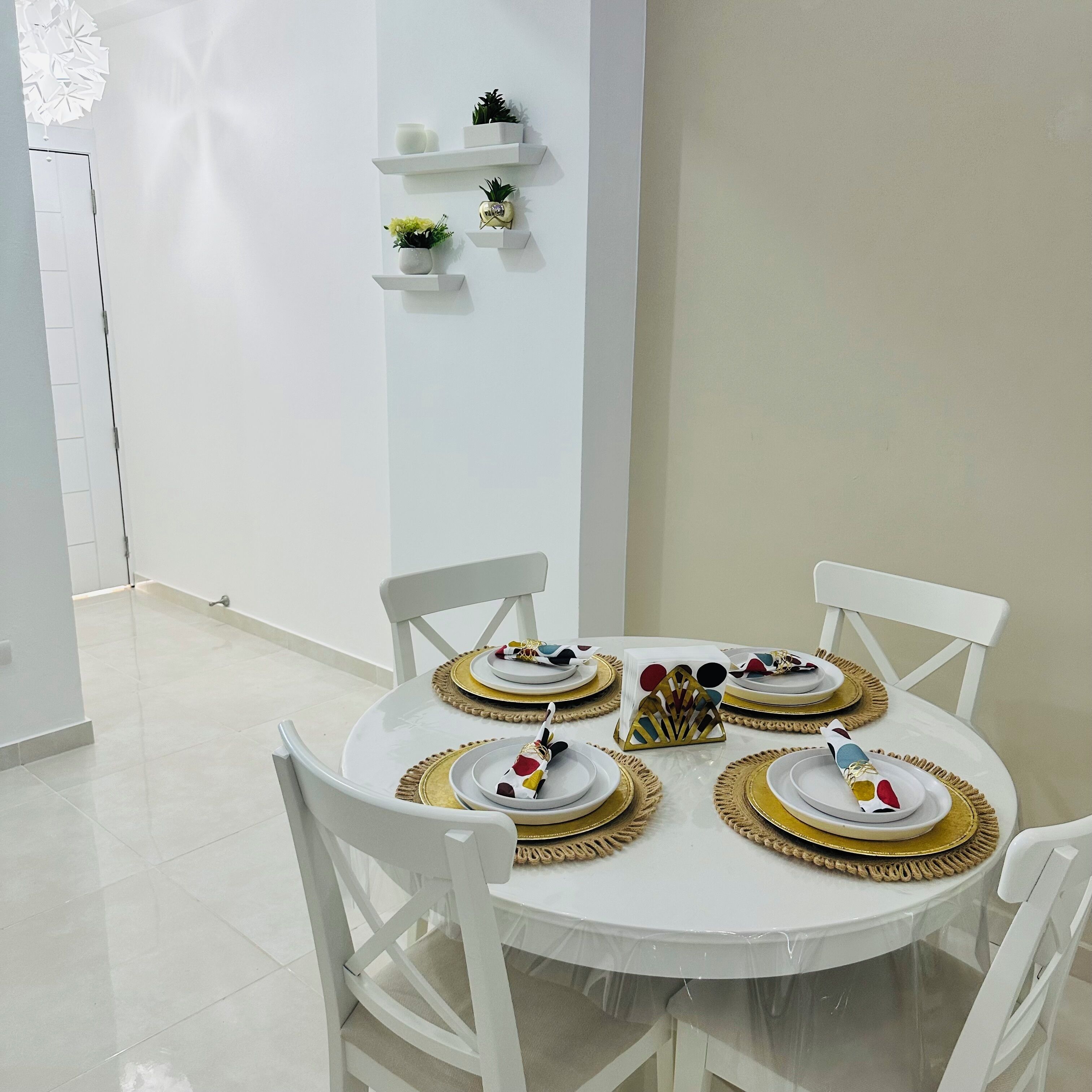 Een eetruimte met een ronde tafel voor vier personen, witte stoelen en borden met een gouden rand.