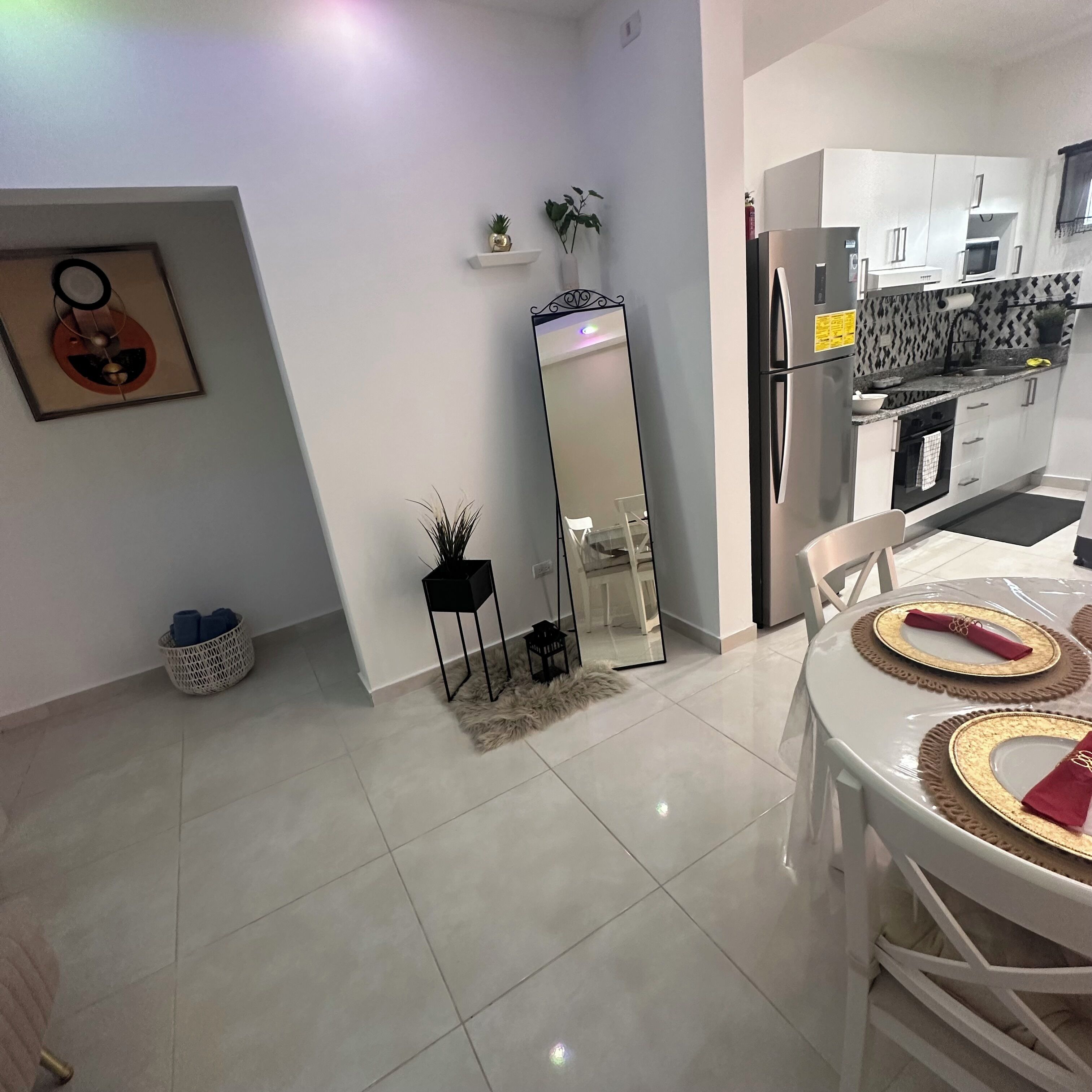 A modern kitchen with white cabinets, a stainless steel refrigerator, and a dining area with a round table set for two.