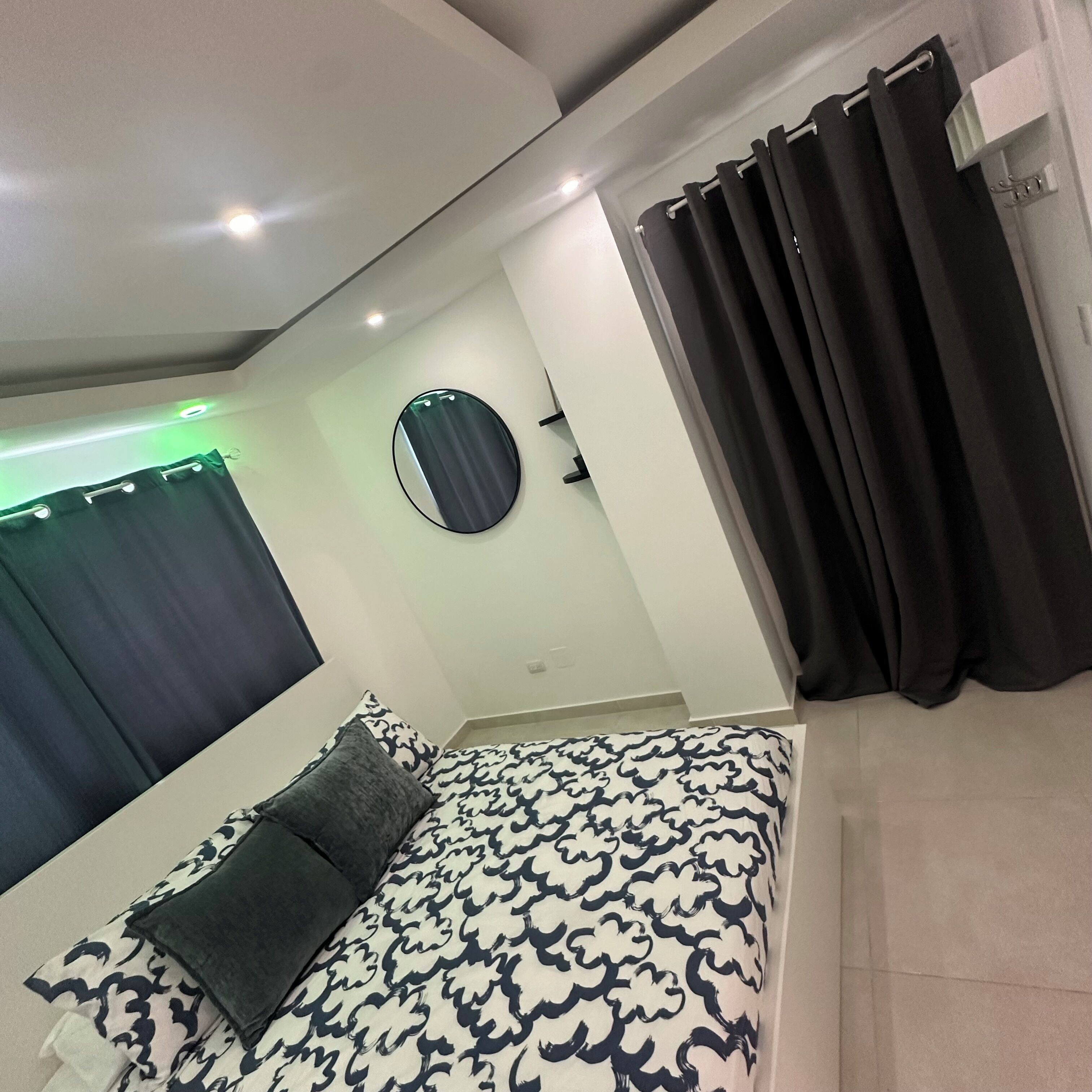 Un dormitorio moderno con cama, un espejo redondo y cortinas negras.