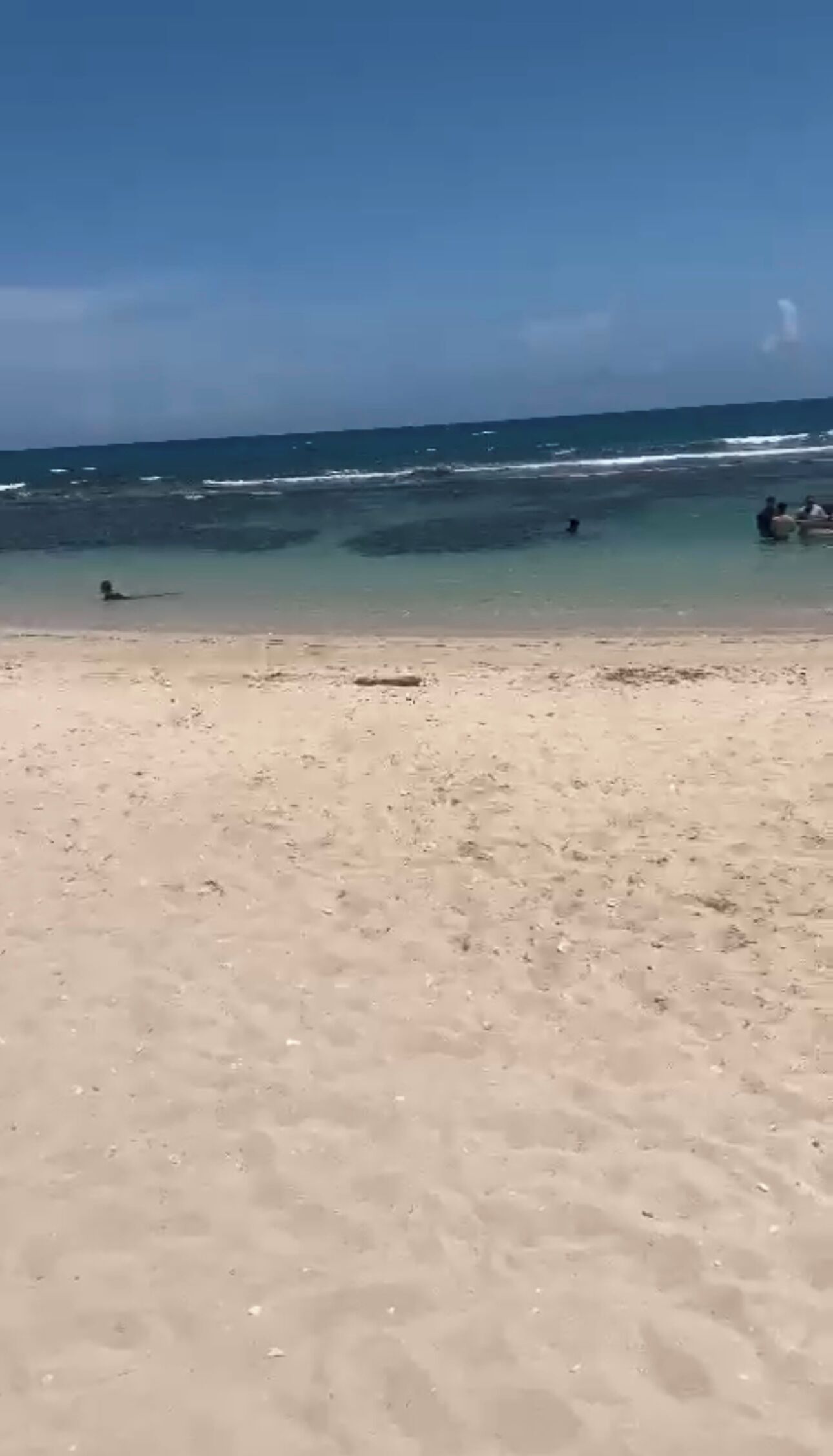 A beach with clear water and a few people in the distance.