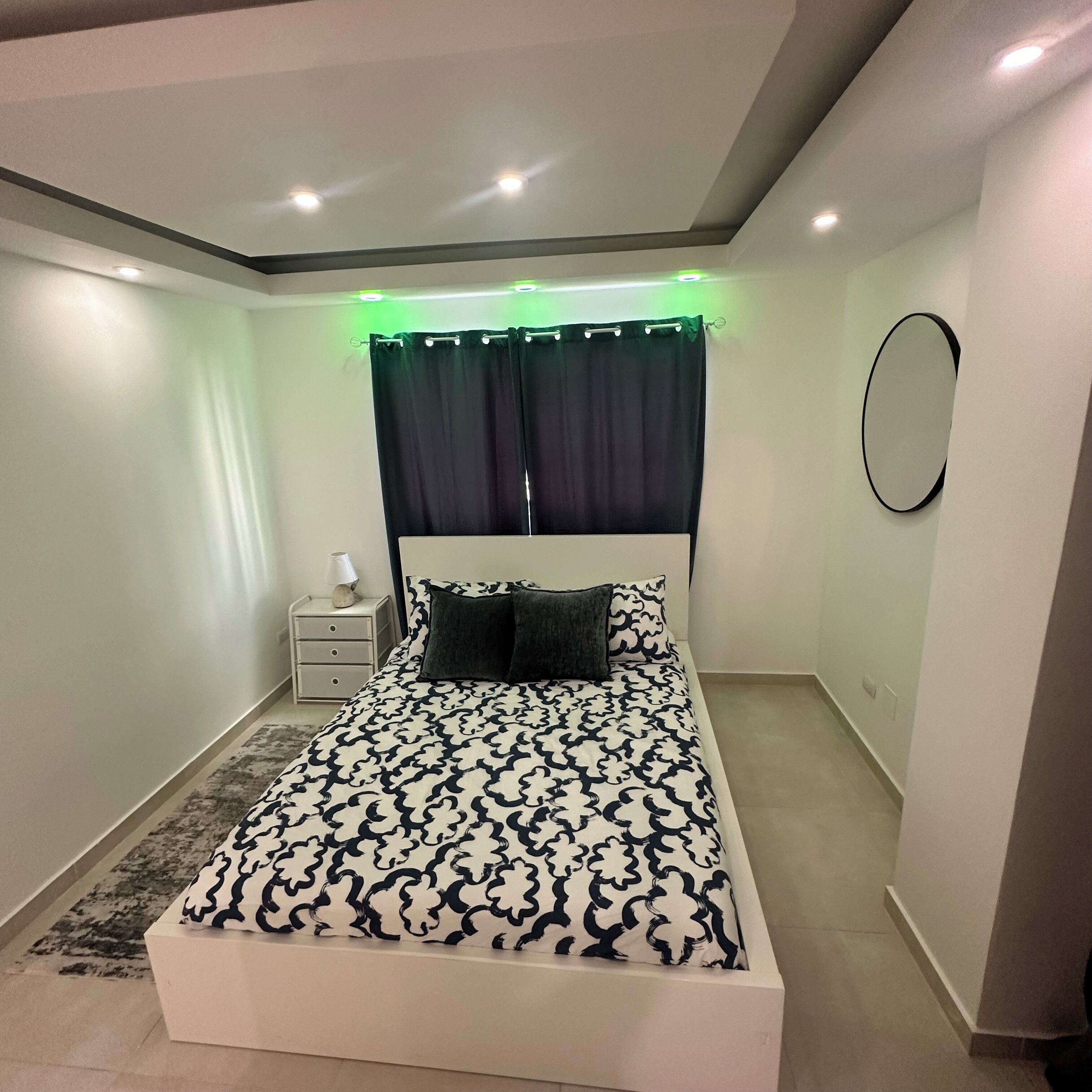 Un dormitorio moderno con una cama grande, una mesita de noche, una lámpara y un espejo en la pared.