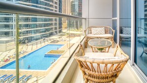 Un balcón con mobiliario de mimbre que da a una piscina y edificios altos.
