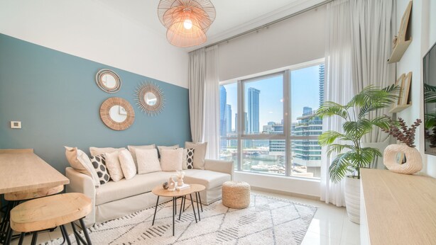 Una sala de estar moderna con un sofá, una mesa de centro y vistas de la ciudad a través de amplios ventanales.