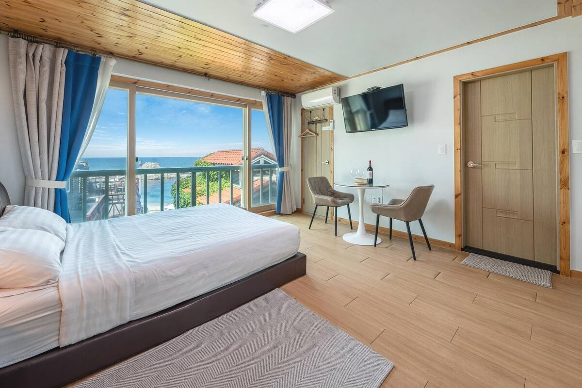 Une chambre avec un lit, une télévision, une petite table avec des chaises et un balcon avec vue.