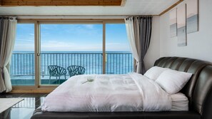 A bedroom with a large bed, a view of the sea through a balcony, and a dining area with chairs.
