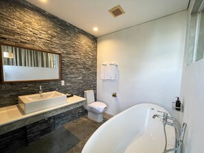 A modern bathroom with a stone wall, a large bathtub, a sink, and a toilet. - Talent Residence (Phnom Penh)