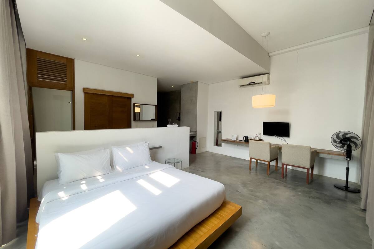 Une chambre d’hôtel moderne équipée d’un grand lit, d’un bureau, d’une chaise, d’une télévision et d’un ventilateur.