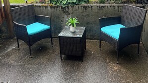 An outdoor seating area with two wicker chairs and a small table, surrounded by a concrete wall and various plants. - Cozy 1 bedroom apartment in Enjoyable Ketchikan with WiFi.  (Ketchikan)