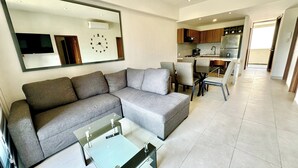 A modern living room with a sectional sofa, a glass coffee table, and a kitchen in the background.