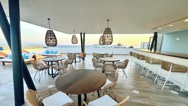 A rooftop bar with wicker furniture, a bar counter, and hanging light fixtures.