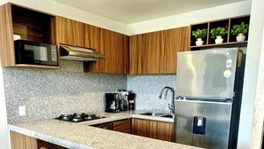 A modern kitchen with wooden cabinets, a granite countertop, stainless steel appliances, and two bar stools.