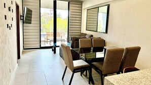 A modern dining area with a glass table, six chairs, and a large window with blinds.