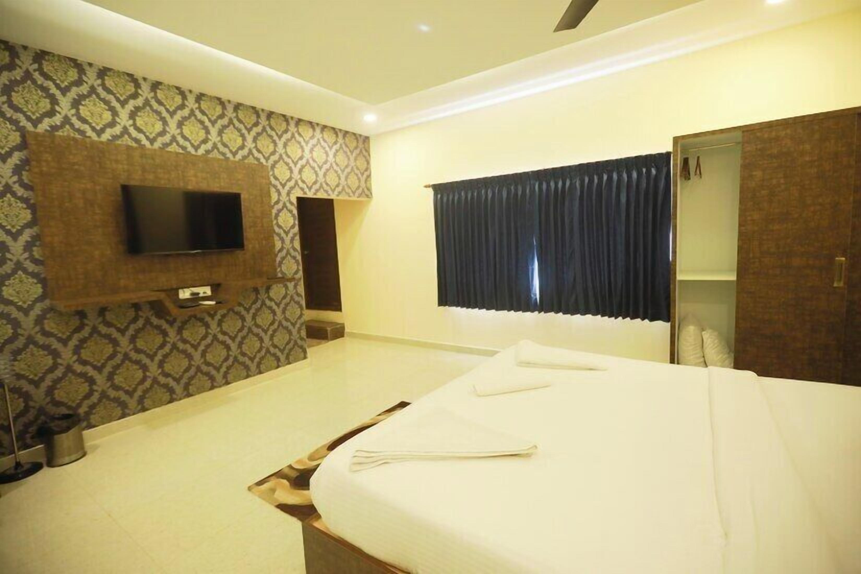A hotel room with a bed, a TV mounted on the wall, a wardrobe, and a window with curtains.