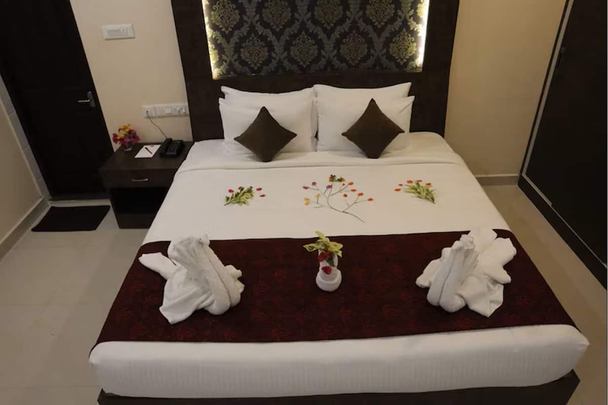 A neatly made bed with a floral bedspread, two pillows, and a vase with flowers.
