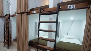 Bunk beds with wooden ladders, a small shelf, and a white wall with a window.