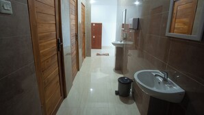A narrow hallway with wooden doors, a sink, and a trash can.