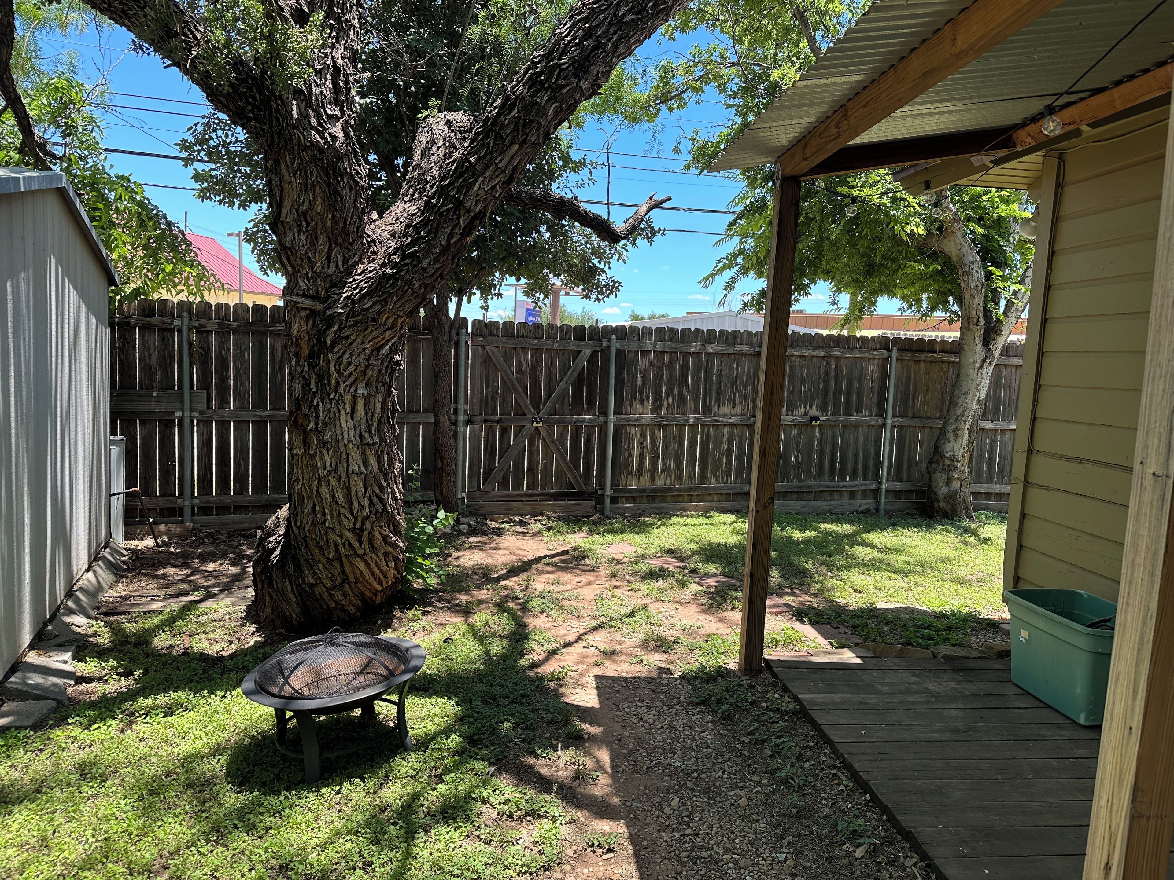 A backyard with a wooden deck, a tree, a metal chair, and a fenced area.