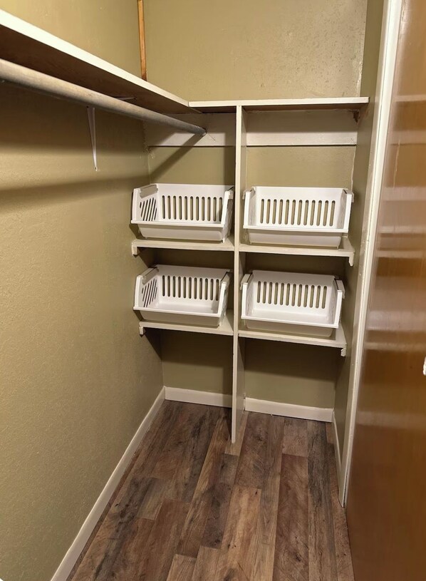 A storage closet with wooden flooring and white shelves.
