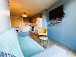 A compact living space with a sofa, a yellow armchair, a small round table, a kitchen area with appliances, and a mounted TV. - Gulf of St-Tropez Studio/Cabin for 4 People (GASSIN)