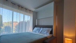 A hotel room with a bed, a nightstand with a lamp, and a window with curtains.