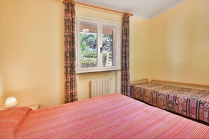 Um quarto com uma cama, janela com cortinas, radiador e luminária.