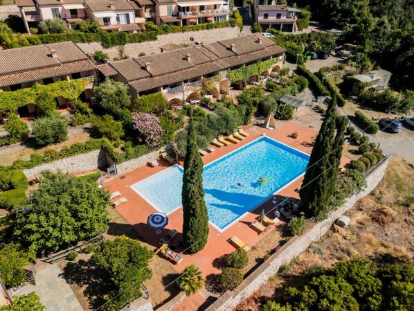 Vista aérea de uma área residencial com piscina, cercada por cadeiras de sol e guarda-sóis, sugerindo um ambiente de resort.