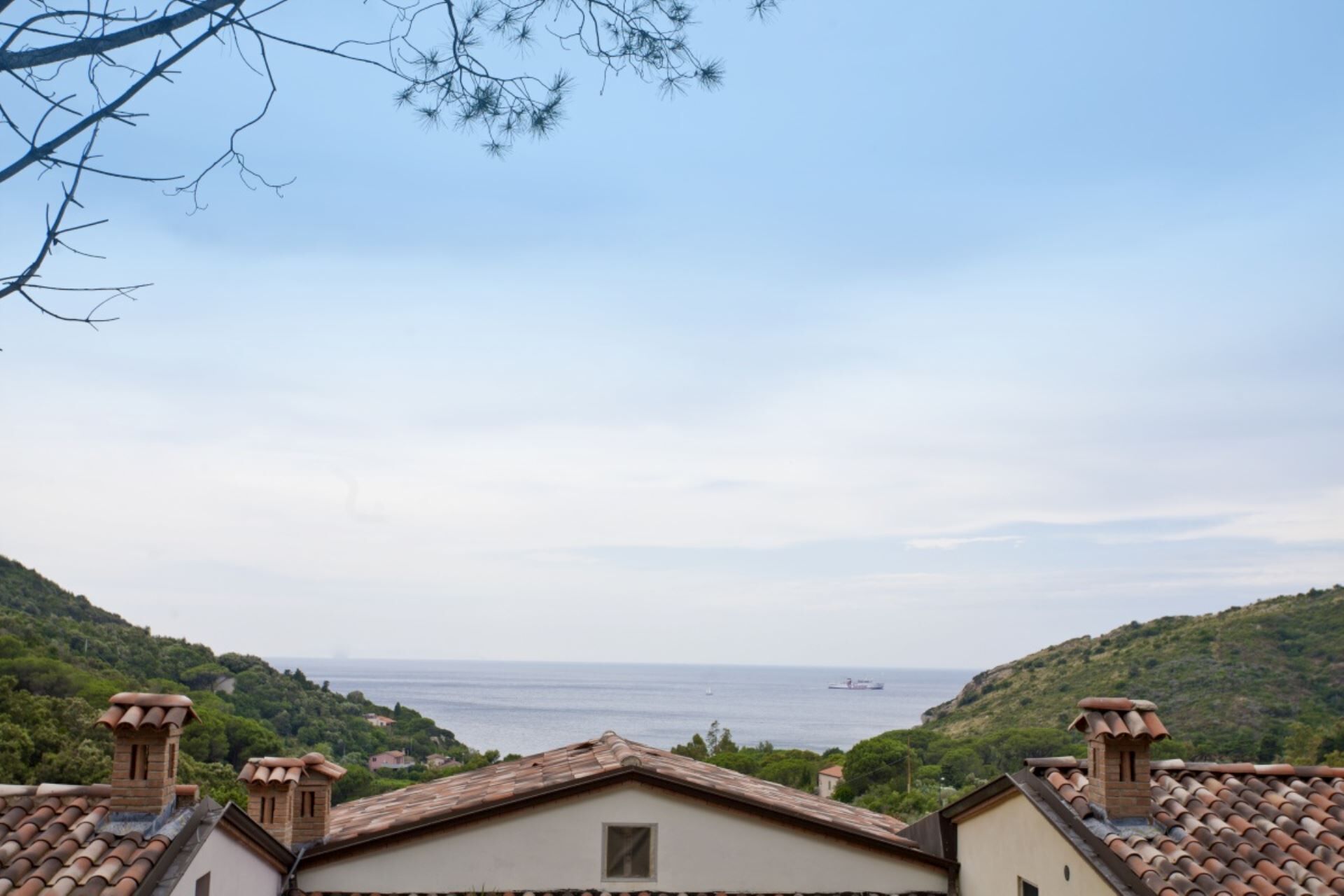 Vista costera con tejados de teja terracota, cielo despejado y una lejanía del mar.