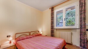 A bedroom with a bed, a nightstand, a lamp, a window with curtains, and a radiator. - RELAIS NISPORTINO - BORGO ALLORO 58 (Rio dell'Elba)
