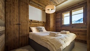 Een slaapkamer met houten lambrisering, een bed, een raam en een hanglamp.