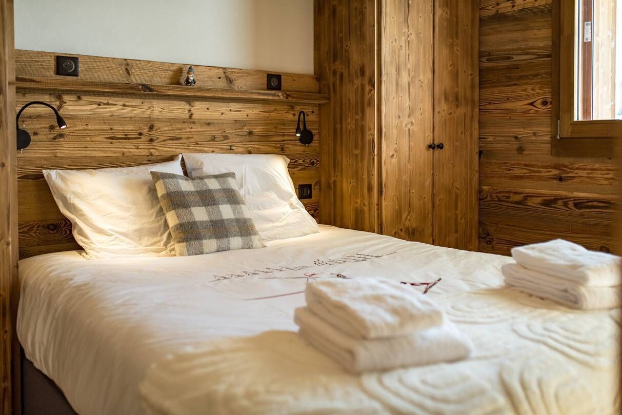 A wooden-paneled room with a bed, two wall-mounted lamps, and a window.