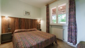 A bedroom with a wooden headboard, a bed with patterned bedding, a window with curtains, and a radiator.
