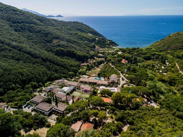 An aerial view of a coastal village with terraced houses, a small beach, and a clear view of the sea.