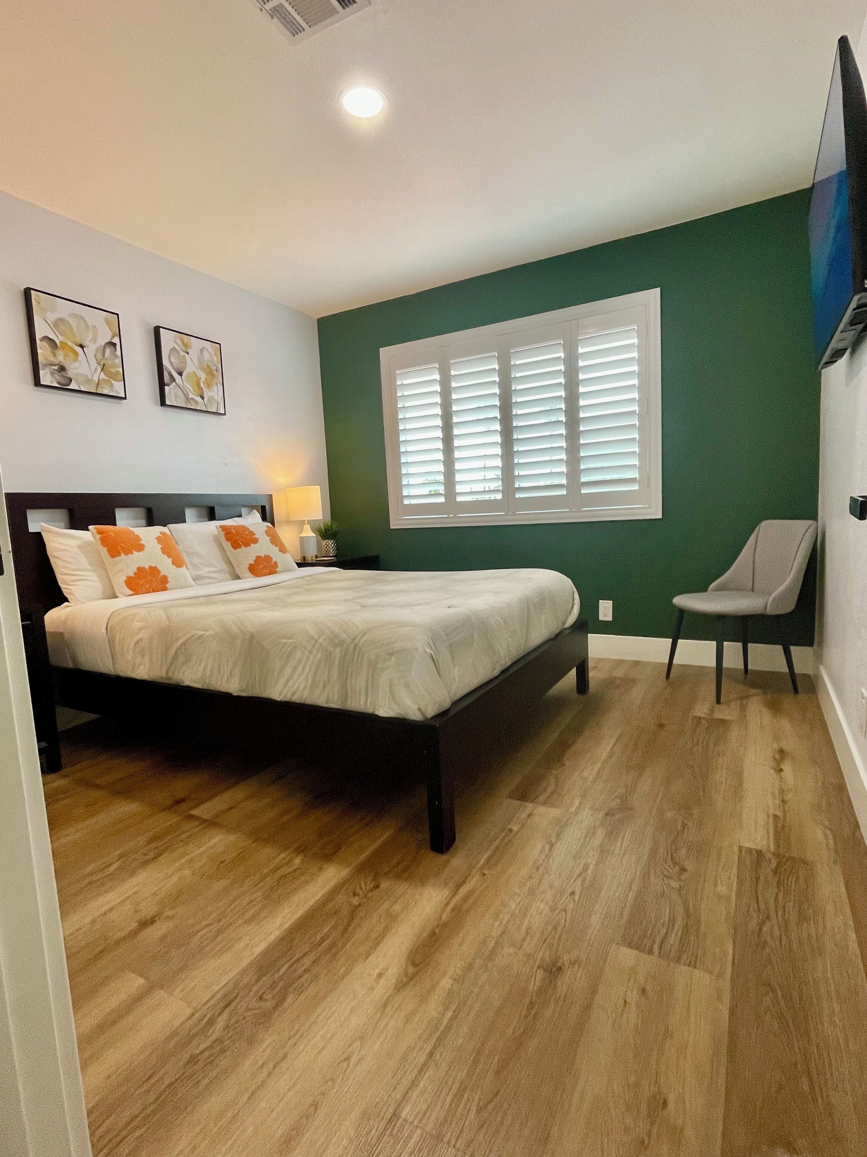 Ein Schlafzimmer mit einem Bett, einem Sessel, einem Fenster mit Jalousien und Bildern an der Wand.