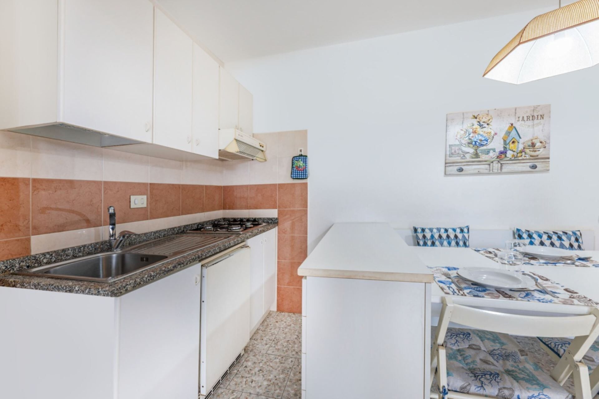 A compact kitchen with white cabinets, a granite countertop, and a small dining area with a table and chairs.